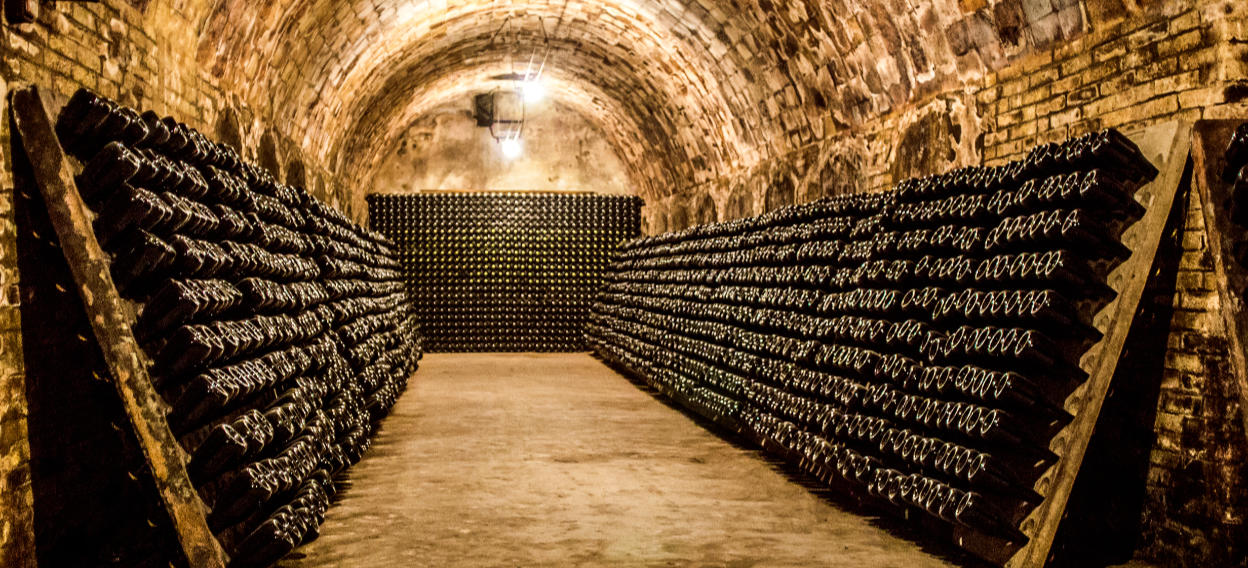 Rows of aging wine bottles rest in a dimly lit, vaulted stone cellar beneath a historic French winery. This image reflects the artisanal wine heritage and exclusive tasting experiences at the heart of Vivida's Champagne & Burgundy tour.